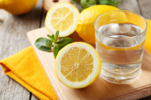 Lemons on cutting board with glass of water on grey wooden background